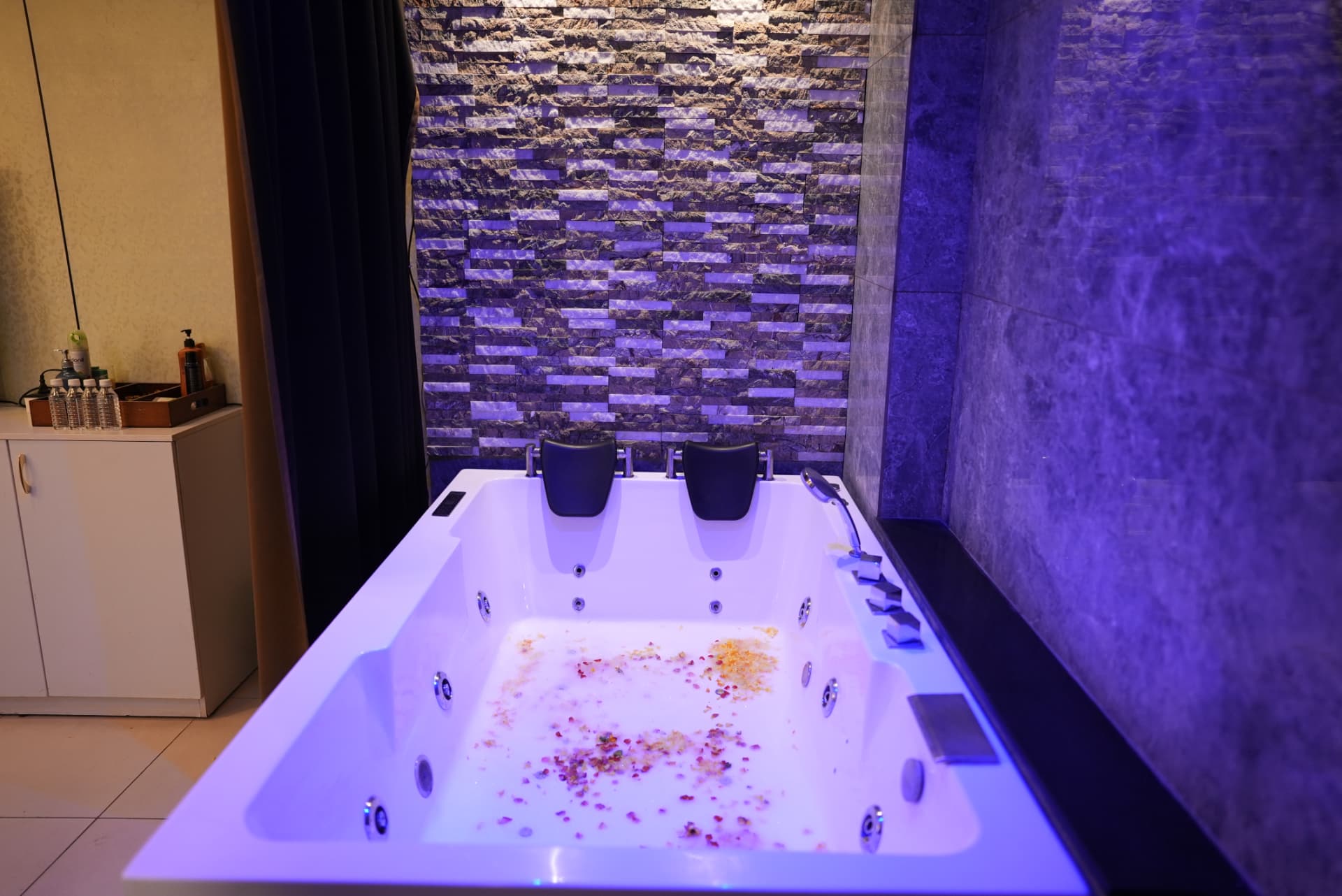 Private couples jacuzzi filled with rose petals under soft violet lighting